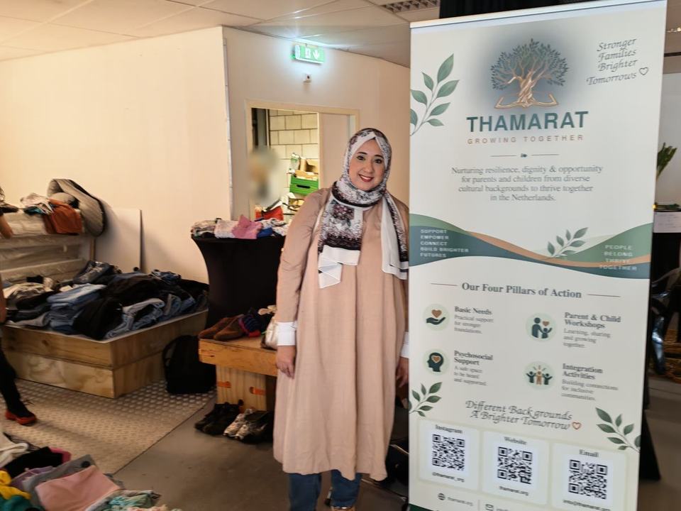 Yara Gamal, Thamarat’s founder, standing beside the Thamarat banner, with clothes on crates and the bazaar behind her.
