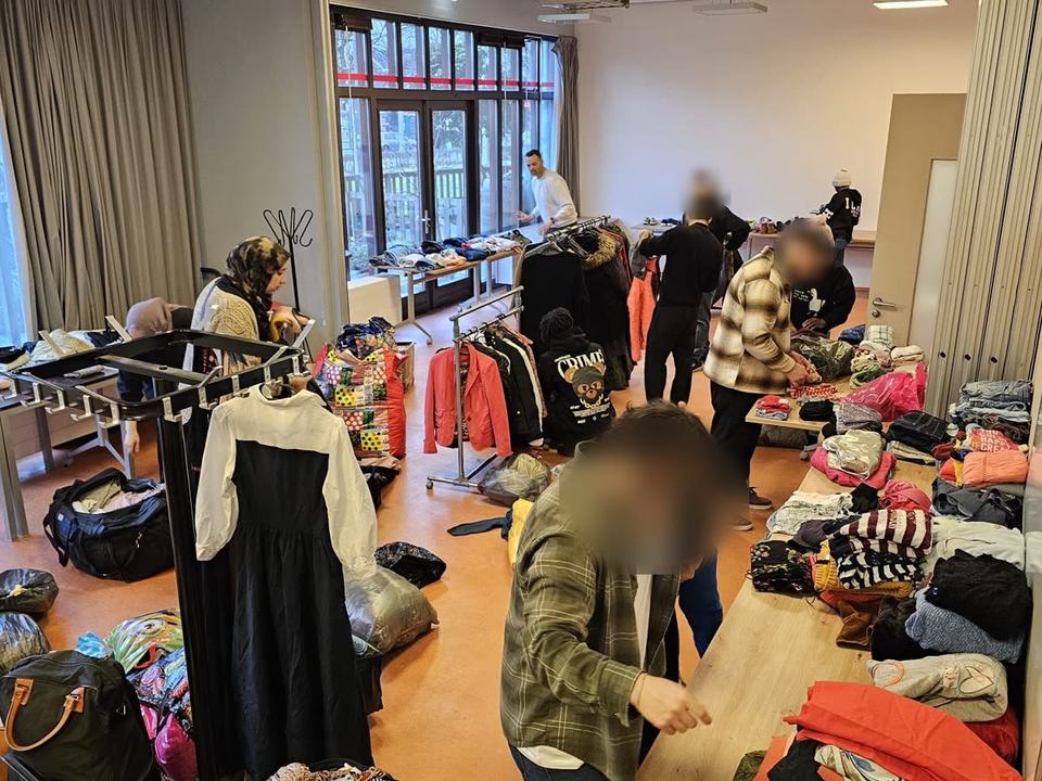 Yara Gamal, our founder, and our co-founder sorting donated clothes onto tables and rails in a community hall with volunteers, with bags of donations on the floor. Some faces are blurred.