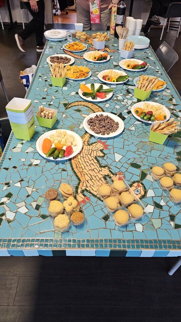 A mosaic table with plates of vegetables, cheese, crisps, breadsticks and biscuits.