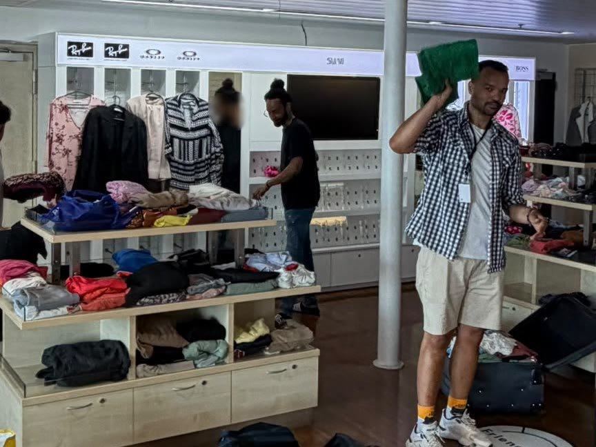 Our co-founder and two volunteers arranging folded clothes on shelves and rails in a shop space on board a ship.