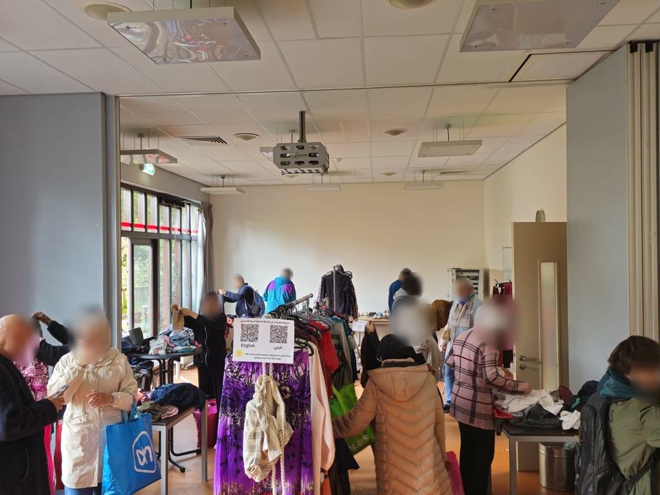 People browsing rails and tables of donated clothes in a large hall.